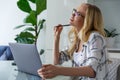 pensive young woman in eyeglasses working with laptop