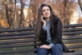 Pensive young woman with long wavy brown hair sits in park on bench and talks on phone and gesticulating Royalty Free Stock Photo