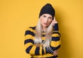 Pensive young woman, model wearing woolen cap and sweater, isolated on yellow background. Girl frowning her face holding finger on Royalty Free Stock Photo