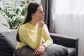 Pensive young woman sitting on couch at home look in distance mourning yearning, unhappy upset girl thinking suffering from Royalty Free Stock Photo