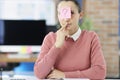 Pensive young woman sitting at table with sticker with question mark on her forehead