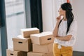 pensive young woman standing with hand on chin and looking at cardboard boxes Royalty Free Stock Photo