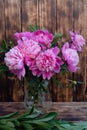 Peony and flower buds in a glass vase. A wooden wall in the background. Flowers on a wooden background