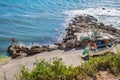 Assenta, PORTUGAL - 4 July 2020 - Wall of rocks with people watching the sea and fishing boat with vegetation in blur