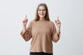 Advertisment concept. Happy woman in sweater, points up with fore fingers as shows something, has surprised pleased