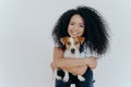 People, animal or pet care concept. Curly haired woman embraces favourite dog, smiles pleasantly, stands against white background