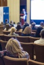 People Attending Business Conference Sitting in Front of the Host Speaking on Stage Against Big Screen. Royalty Free Stock Photo