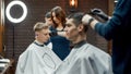 People in barbershop. Side view of a young focused barber girl or female hairdresser making new trendy haircut for Royalty Free Stock Photo