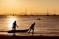 People on the beach play sports in the light of a golden sunset. Kayakers float in the water, two girls carry out to the land of