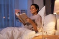 smiling young woman reading book in bed at home Royalty Free Stock Photo