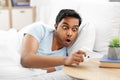 Overslept indian man in bed looking at alarm clock Royalty Free Stock Photo