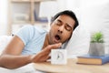 Sleepy indian man with alarm clock in bed yawing