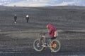 People bike big wheel bicycle on black sand beach with snow cove