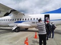 People boarding a small propeller plane from the runway of a tropical airport