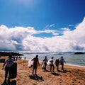 People cleaning the beach with plastic bags of trash and a blue sky in the backgroud