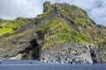 People climbing Gardar basalt columns of Reynisfjall mountain in Southern Iceland. Black sand of Reynisfjara beach in is at