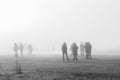 People in coats walking along foggy beach