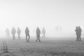 People in coats walking along the foggy beach