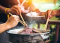 People cooking meat and grill. Food are vegeteble. People use chopsticks.