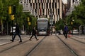 People crossing in front of the slowly moving tram after stopping at its stop.