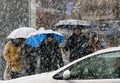 People crossing snowy city street in heavy snowfall and a driving car in front of them