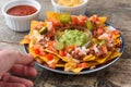 People eating mexican nachos with beef, guacamole, cheese sauce, peppers, tomato and onion in plate on wood