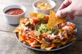 People eating mexican nachos with beef, guacamole, cheese sauce, peppers, tomato and onion in plate on wood