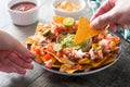 People eating mexican nachos with beef, guacamole, cheese sauce, peppers, tomato and onion in plate on wood