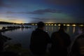 People enjoying faint aurora northern light unther the cloudy starry dark blue sky and water reflection