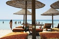 People enjoying together in the colorful turquoise sea water on sunny day in beautiful beach. Straw umbrellas and wooden sunbeds