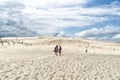 People explore in Lacka dune in Slowinski National Park in Poland. Traveling dune in sunny summer day. Sandy beach and blue sky.