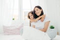 People, family and bedding concept. Cheerful young smiling mother and her daughter embrace each other, have positive expression, w