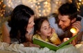 Happy family reading book in bed at night at home