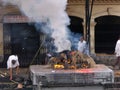 People by the fire of a funeral pyre with a corpse being cremated at the Pashupatinath temple in Kathmandu, Nepal
