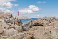 People fishing off craggy shore with red lighthouse in background