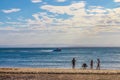 People fishing silhouetted against the water of the bay as a motorboat speeds by with opposite shore barely visible on horizon