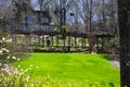 People in the garden walking through a long tunnel of brown wooden awnings surrounded by lush green grass, bare winter trees Royalty Free Stock Photo