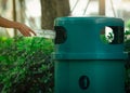 People hand throwing empty water bottle in recycle bin at park. Green plastic recycle bin. Man discard bottle in trash bin. Waste