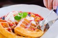 People hand used silver spoon and fork to eat Sweet waffles with strawberries sauce vanilla ice cream and fresh fruit on white pla Royalty Free Stock Photo