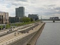 People haning out on a quay along River Rhine, with Severinsbrucke bridge , Kranhaus buildings, and office towers