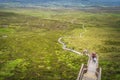 People hiking on wooden boardwalk, climbing on steep steps and stairs to reach Cuilcagh Mountain peak