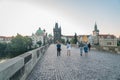People and historic statues at sunrise of famous Charles Bridge against backdrop of city architecture