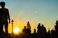 People and historic statues at sunrise of famous Charles Bridge against backdrop of city architecture