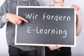 People holding a blackboard with 'we demand e-learning' in German written on it