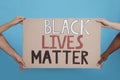 People holding sign with phrase Black Lives Matter on light blue background, closeup. Racism concept