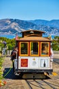 People holding white bar on yellow and red trolley on flat road with ocean and mountains behind