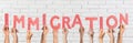 People holding word IMMIGRATION made of cardboard letters near brick wall. Banner design Royalty Free Stock Photo