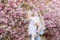 People, holidays and family concept - daughter hugs mom sitting on her back on cherry blossom background. Walk in the sakura trees