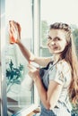 People, housework and housekeeping concept - happy woman in gloves cleaning window with rag and cleanser spray at home Royalty Free Stock Photo