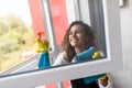 People, housework and housekeeping concept - happy woman in gloves cleaning window with rag and cleanser spray at home Royalty Free Stock Photo